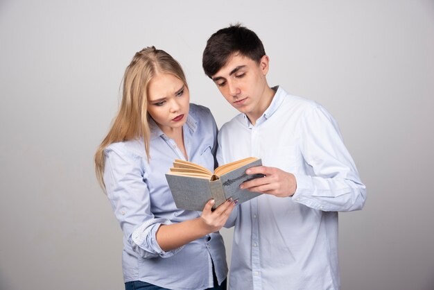 Jeune couple debout avec livre sur fond gris