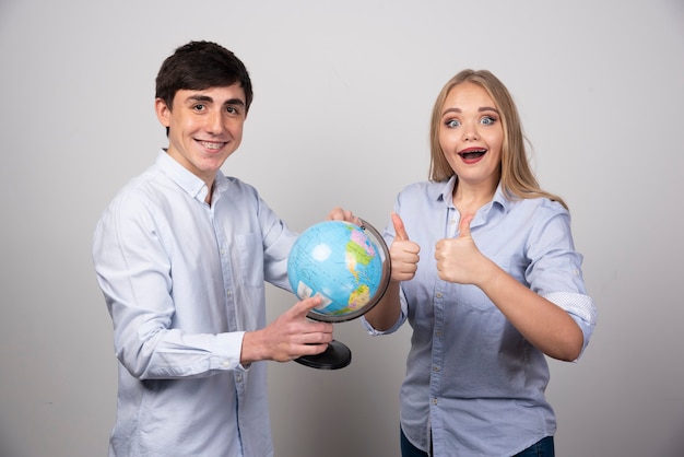 Photo gratuite jeune couple debout et posant avec un globe terrestre