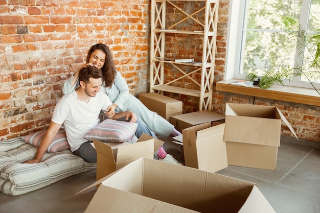 Jeune couple a déménagé dans une nouvelle maison ou un nouvel appartement. Allongé ensemble, caddling, étreindre, s'amuser le jour du déménagement. Ayez l'air heureux, rêveur et confiant. Famille, déménagement, relations, premier concept de maison.