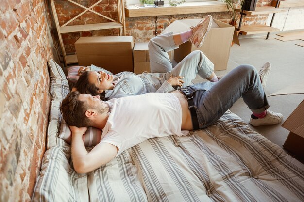 Jeune couple a déménagé dans une nouvelle maison ou un nouvel appartement. Allongé ensemble, se détendre après le nettoyage et le déballage le jour du déménagement. Ayez l'air heureux, rêveur et confiant. Famille, déménagement, relations, premier concept de maison.