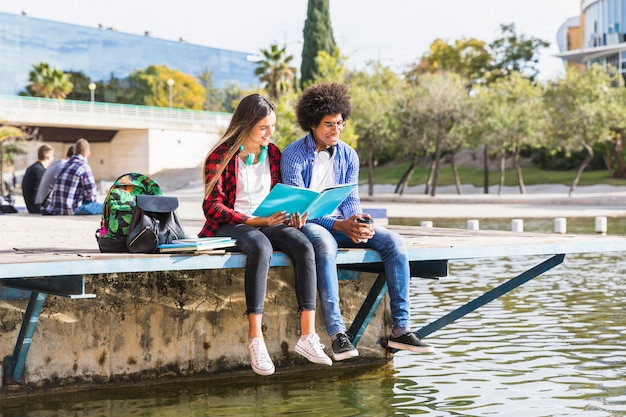 Jeune couple diversifié apprennent ensemble assis dehors dans le parc