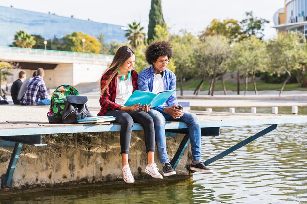 Jeune couple diversifié apprennent ensemble assis dehors dans le parc