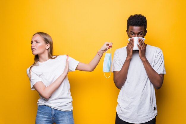 Jeune couple diversifié, homme éternue femmes choquées isolées sur un mur jaune studio