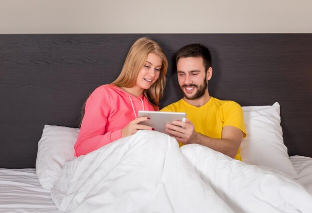 Jeune couple doux sur le lit en regardant quelque chose sur le gadget de la tablette. Concept sur la technologie et les gens