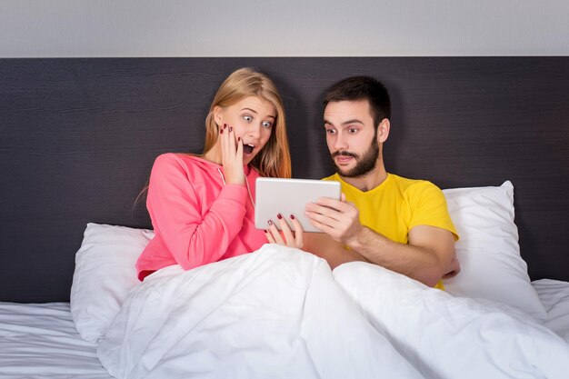 Jeune couple doux sur le lit en regardant quelque chose sur le gadget de la tablette. Concept sur la technologie et les gens