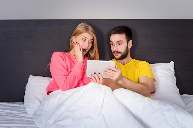 Jeune couple doux sur le lit en regardant quelque chose sur le gadget de la tablette. Concept sur la technologie et les gens