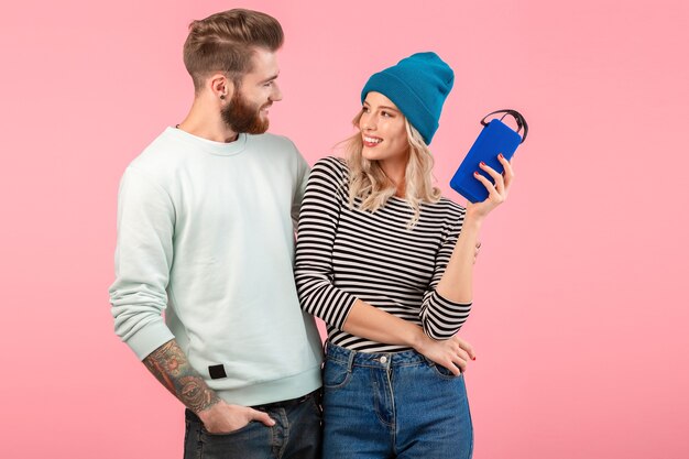 Jeune couple écoutant de la musique sur haut-parleur sans fil portant une tenue élégante et cool souriant posant sur rose