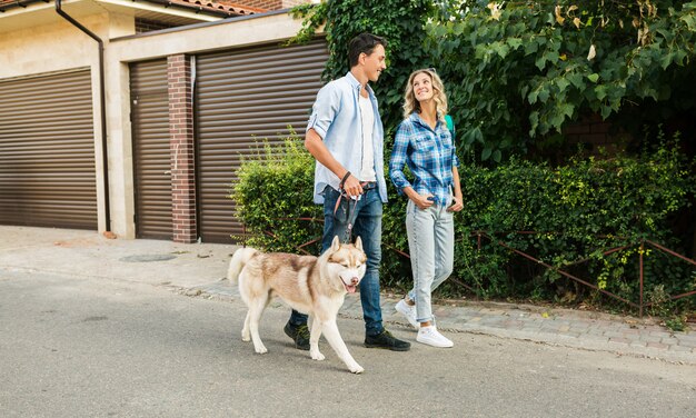 Jeune couple élégant marchant avec un chien dans la rue. homme et femme heureux avec race husky