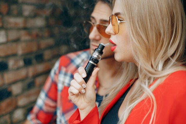 Jeune couple élégant avec vape dans une ville