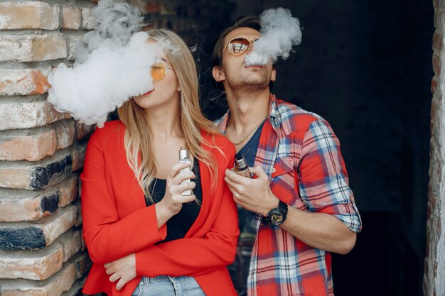 Jeune couple élégant avec vape dans une ville