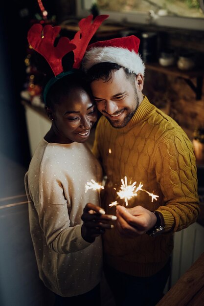 Jeune couple embrassé utilisant des cierges magiques et s'amusant le soir du Nouvel An à la maison