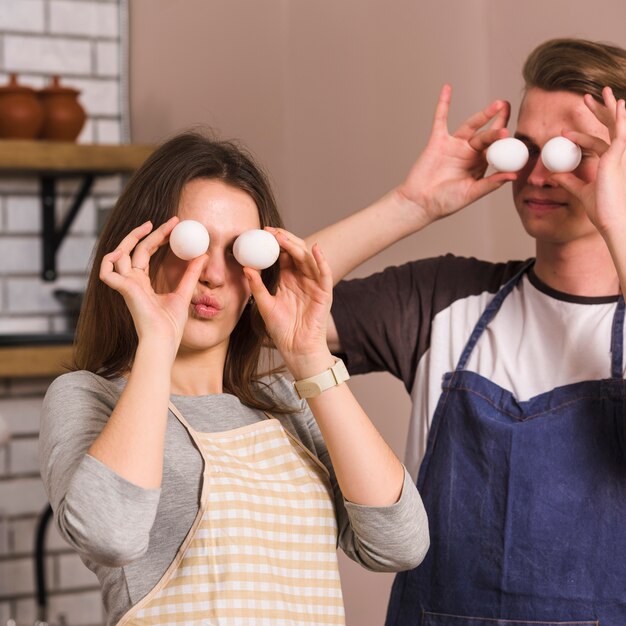 Jeune couple faisant des grimaces avec des oeufs dans la cuisine