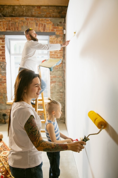 Jeune couple, famille faisant la réparation d'appartement ensemble eux-mêmes. Mère, père et fils faisant la rénovation ou la rénovation de la maison. Concept de relations, de mouvement, d'amour. Préparation du mur pour le papier peint