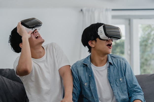 Jeune couple gay asiatique utilisant une technologie amusante à la maison, mec amant de l'Asie lgbtq + se sentant heureux de s'amuser et de la réalité virtuelle, VR jouant à des jeux ensemble tout en restant allongé sur un canapé dans le salon à la maison.