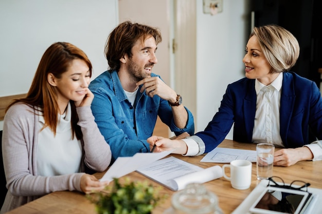 Jeune couple heureux et agent d'assurance parlant tout en analysant les documents lors des consultations.