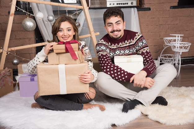 Jeune couple heureux assis avec des cadeaux de Noël près des boules d'argent festives.