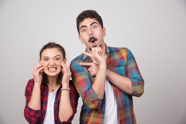 Jeune couple heureux debout et posant sur un mur gris.