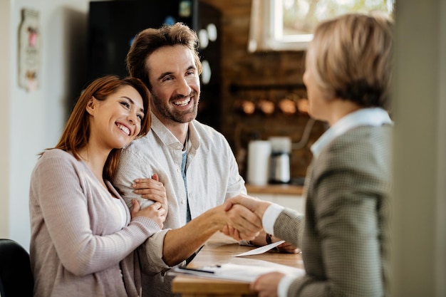 Photo gratuite un jeune couple heureux est parvenu à un accord avec leur agent d'assurance. l'accent est mis sur l'homme serrant la main de l'agent.