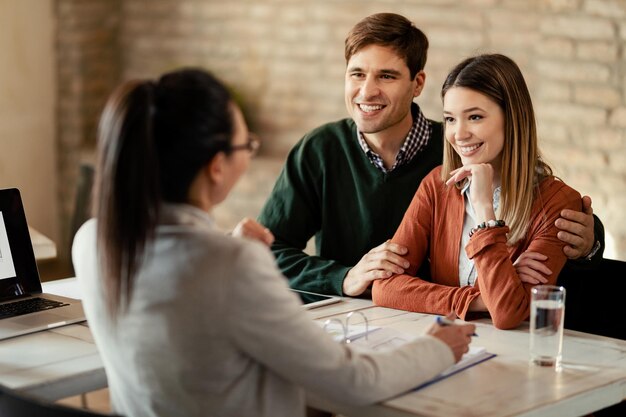 Jeune couple heureux parlant à un conseiller financier lors d'une réunion au bureau