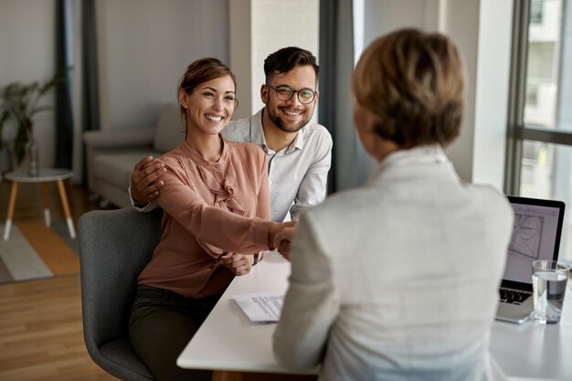 Jeune couple heureux serrant la main d'un agent d'assurance lors d'une réunion au bureau