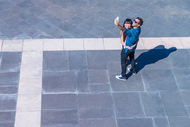 Jeune Couple Heureux Utilisant Un Smartphone Assis Dans La Rue. Prendre Un Selfie Photo Premium