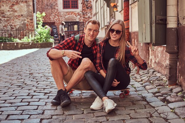 Jeune couple hipster heureux, se reposer pendant une promenade assis sur le trottoir dans la vieille rue de l'Europe.