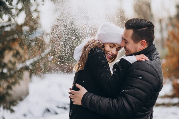 Jeune couple en hiver sous la neige qui tombe de l'arbre