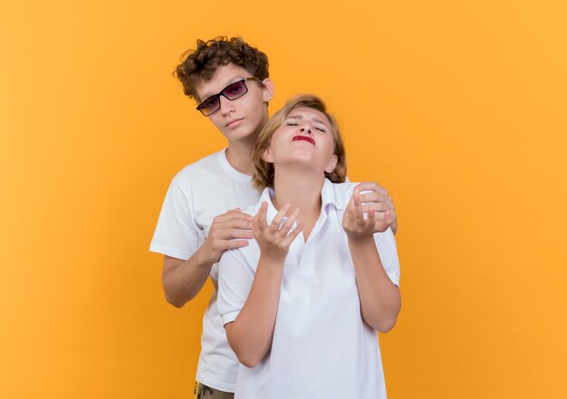 Jeune couple homme essayant de serrer dans ses bras sa petite amie mécontente et bouleversée debout sur un mur orange