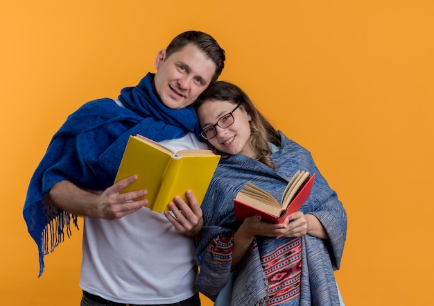 Jeune Couple Homme Et Femme Avec Des Couvertures Tenant Des Livres Heureux Et Positif Souriant Debout Ensemble Sur Un Mur Orange