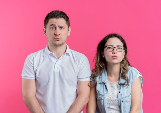 Jeune couple homme et femme dans des vêtements décontractés confus debout sur un mur rose