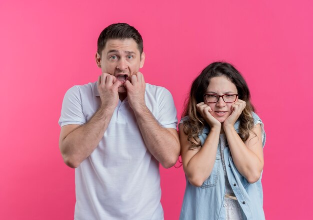 Jeune couple homme et femme dans des vêtements décontractés a souligné et nerveux mordant les ongles sur rose