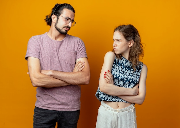 Jeune couple homme et femme fronçant les sourcils se regardant debout sur un mur orange