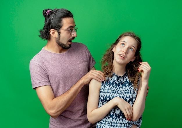 Jeune couple homme et femme, homme surpris touchant l'épaule de sa petite amie qui debout avec une expression pensive debout sur un mur vert