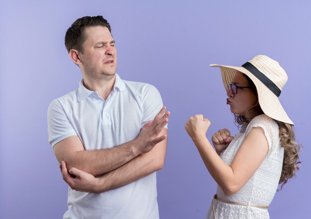 Jeune couple homme et femme se quereller femme avec les poings regardant avec visage en colère à son petit ami alors qu'il montrant panneau d'arrêt debout sur le mur bleu