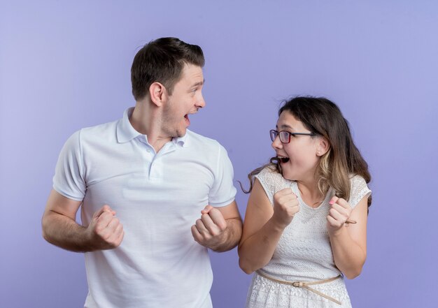 Jeune couple homme et femme serrant les poings heureux et excité debout sur le mur bleu