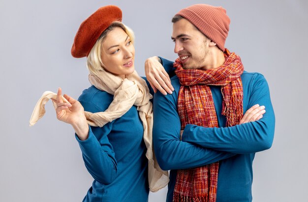 Jeune couple impressionné le jour de la Saint-Valentin portant un chapeau avec une écharpe se regardant isolé sur fond blanc