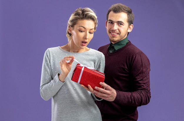 Jeune couple le jour de la saint-valentin heureux gars donnant une boîte-cadeau à une fille surprise isolée sur fond bleu