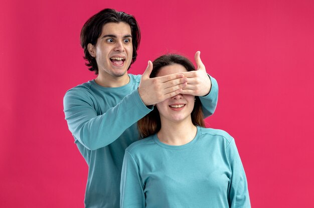 Jeune couple le jour de la Saint-Valentin mec excité a couvert les yeux des filles avec les mains isolées sur fond rose