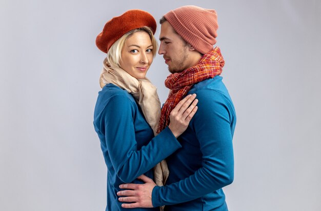 Jeune couple le jour de la Saint-Valentin portant un chapeau avec une écharpe embrassé isolé sur fond blanc