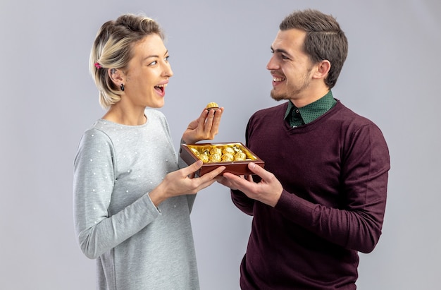 Jeune couple le jour de la Saint-Valentin smiling guy donnant boîte de bonbons à une fille souriante isolée sur fond blanc