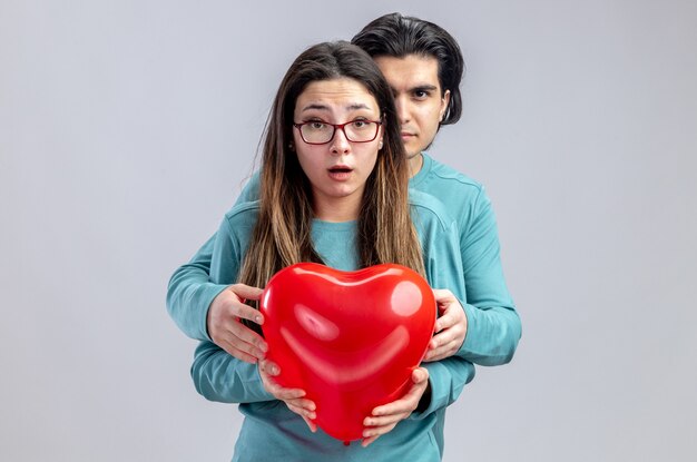 Jeune couple le jour de valentines guy confiant debout derrière fille avec ballon coeur isolé sur fond blanc