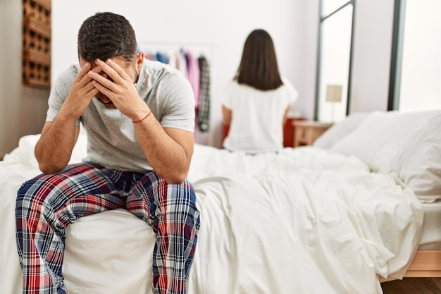 Photo gratuite jeune couple latin en difficulté assis sur le lit avec les mains sur la tête