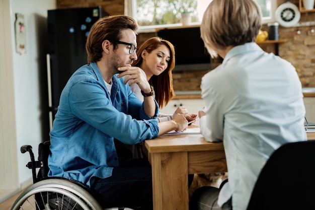 Jeune couple et leur conseiller financier à l'aide d'une tablette numérique lors de la réunion à la maison L'homme est en fauteuil roulant