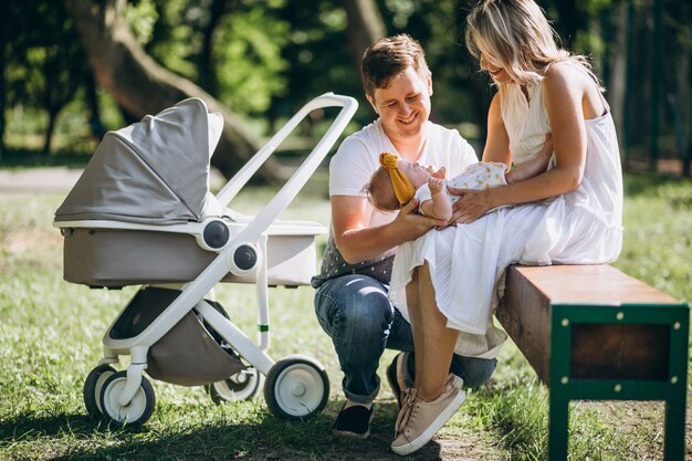 Jeune couple avec leur fille de bébé dans le parc assis par landau