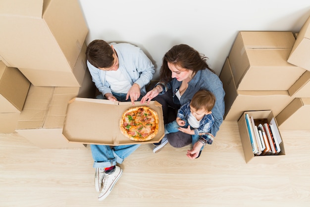 Photo gratuite jeune couple avec leur fils en train de manger la pizza dans leur nouvelle maison