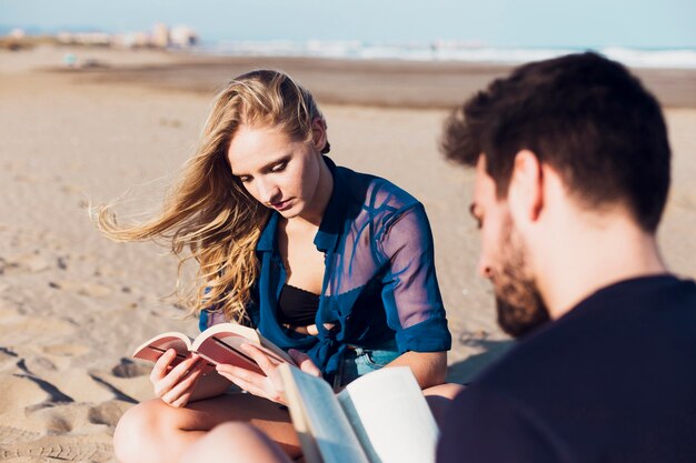 Photo gratuite jeune couple lisant sur la plage