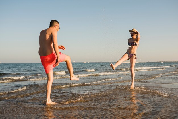 Jeune couple en maillot de bain éclaboussant l&#39;eau à la plage