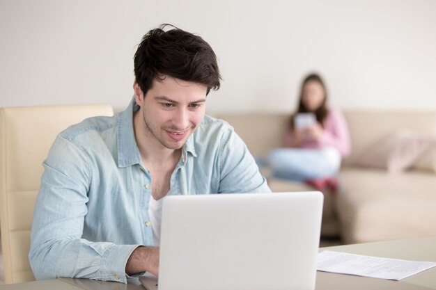 Jeune couple à la maison, homme avec ordinateur portable, femme à l&#39;aide de tablette