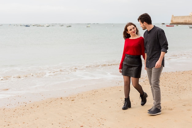 Photo gratuite jeune couple marchant et parlant au bord de la mer