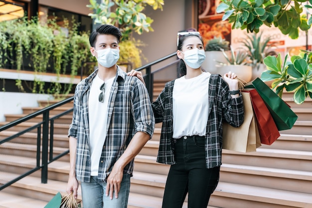 Jeune couple en masque de protection tenant plusieurs sacs en papier
